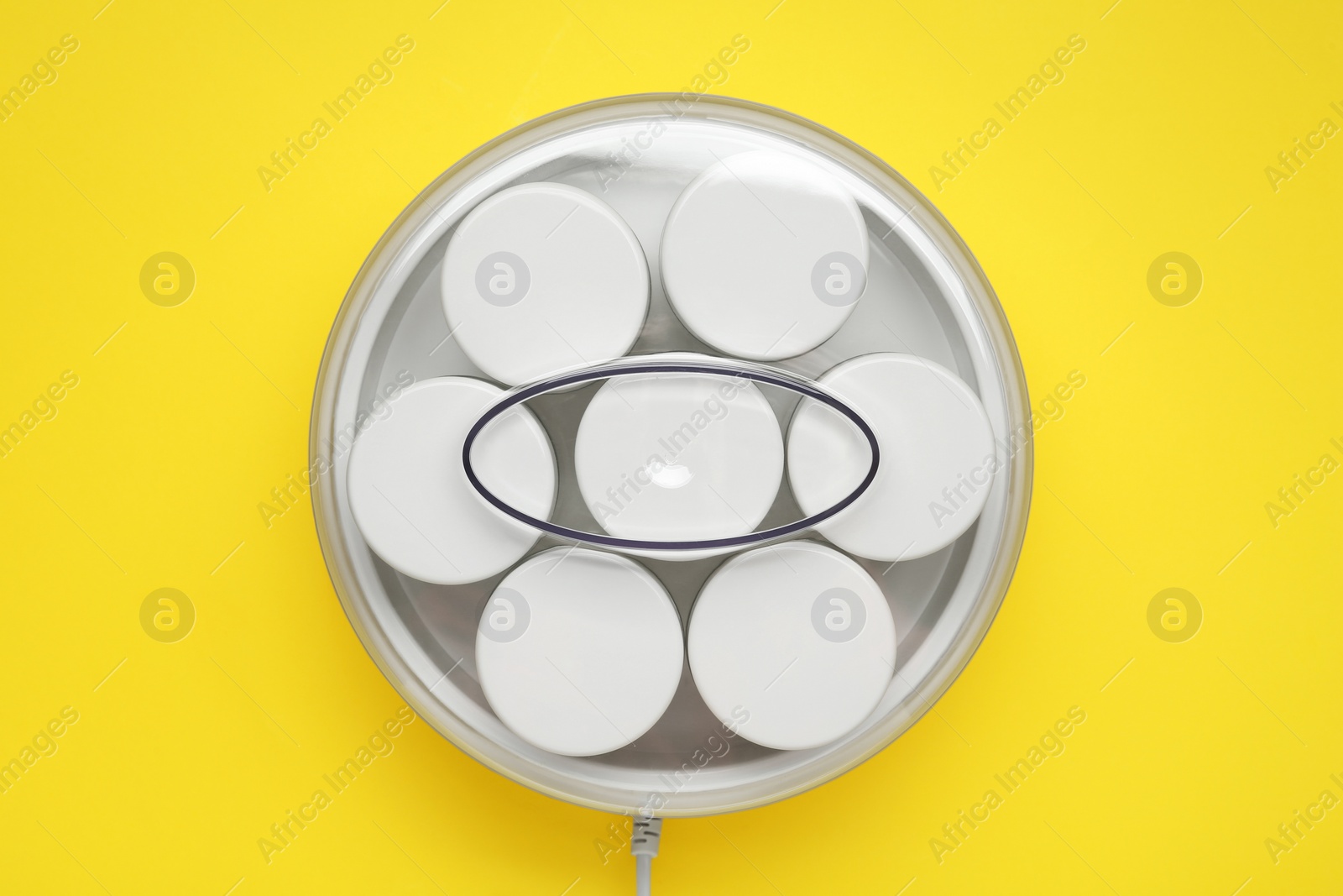 Photo of Modern yogurt maker with jars on yellow background, top view