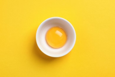 Photo of Bowl with raw egg yolk on yellow background, top view