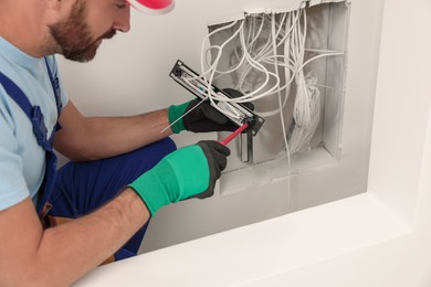 Photo of Electrician with screwdriver fixing patch panel indoors, closeup