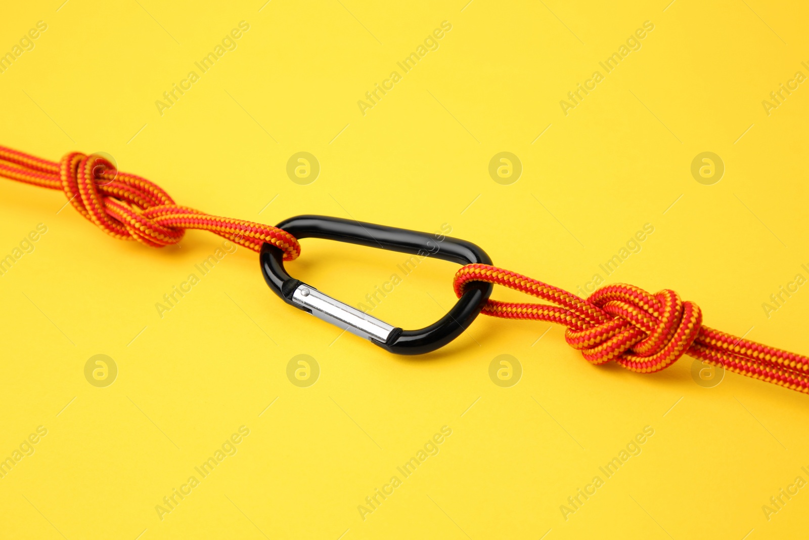 Photo of One metal carabiner with ropes on yellow background