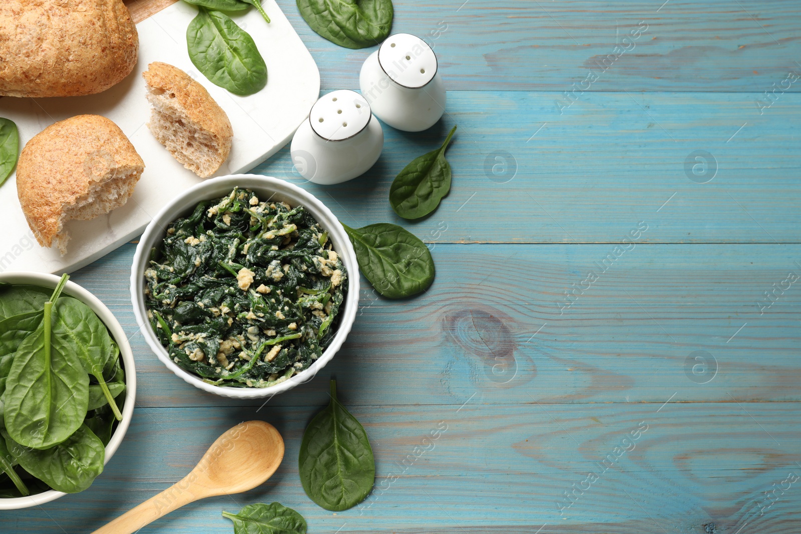 Photo of Tasty spinach dip with egg in bowl, bread and spoon on light blue wooden table, flat lay. Space for text