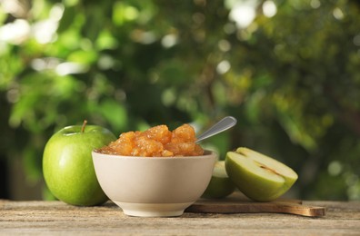 Photo of Bowl with delicious apple jam and fresh fruits on wooden table against blurred background, space for text