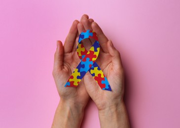 Image of World Autism Awareness Day. Woman with colorful puzzle ribbon on pink background, top view