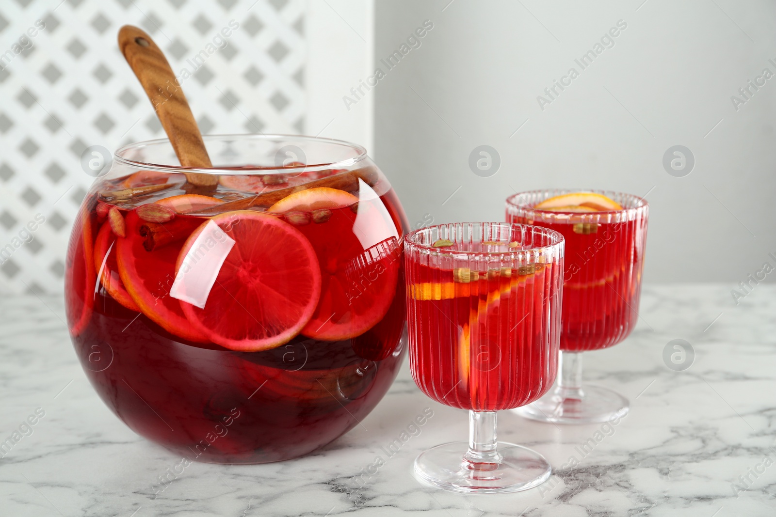 Photo of Glasses and bowl with aromatic punch drink on white marble table