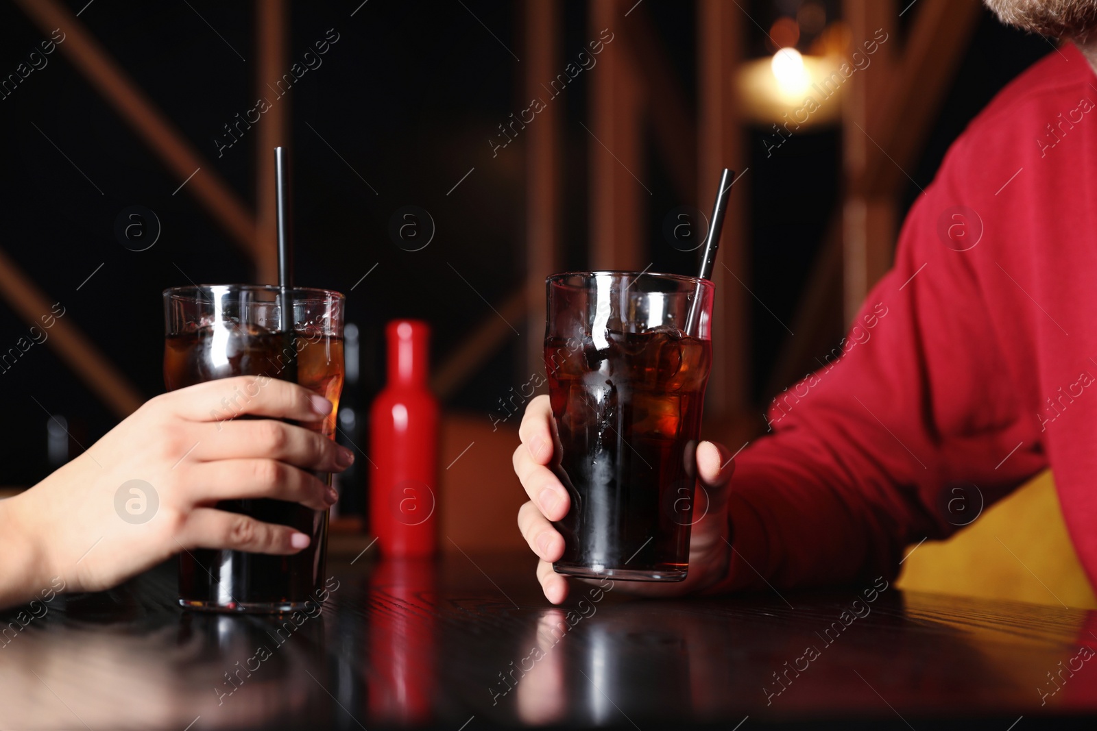 Photo of Young couple with glasses of refreshing cola at table indoors, closeup