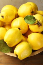 Tasty ripe quince fruits in bowl on wooden table, closeup