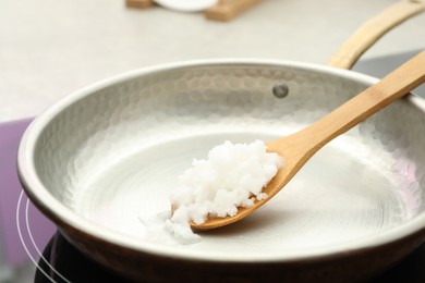 Photo of Frying pan with coconut oil on induction stove, closeup. Healthy cooking