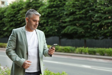 Photo of Portrait of handsome mature man using mobile phone outdoors. Space for text