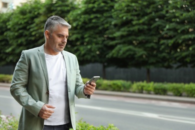 Portrait of handsome mature man using mobile phone outdoors. Space for text