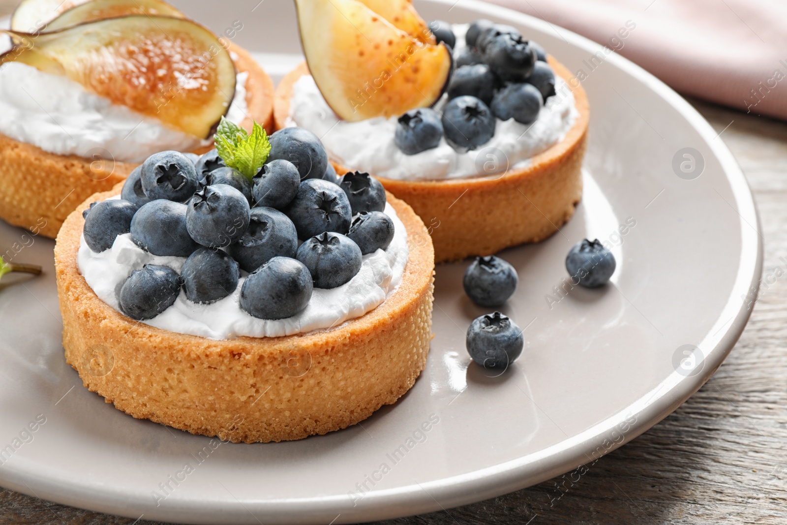 Photo of Plate of tarts with blueberries and figs on wooden table, closeup. Delicious pastries