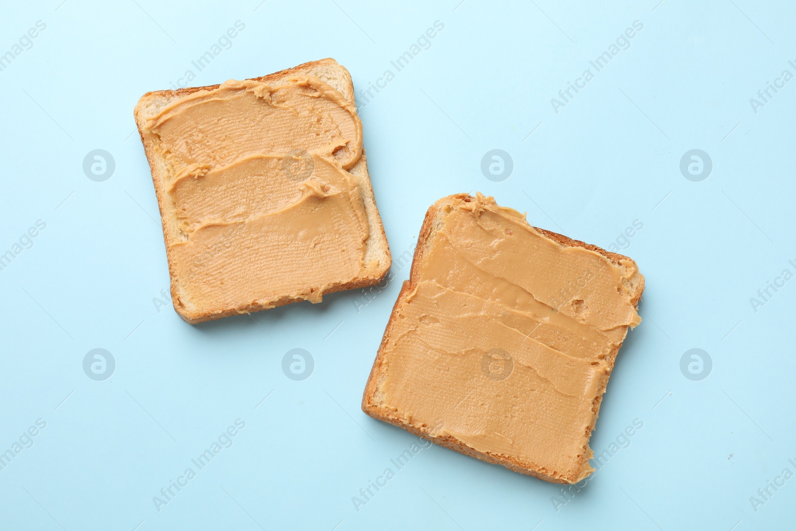 Photo of Tasty peanut butter sandwiches on light blue background, top view