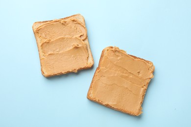 Tasty peanut butter sandwiches on light blue background, top view