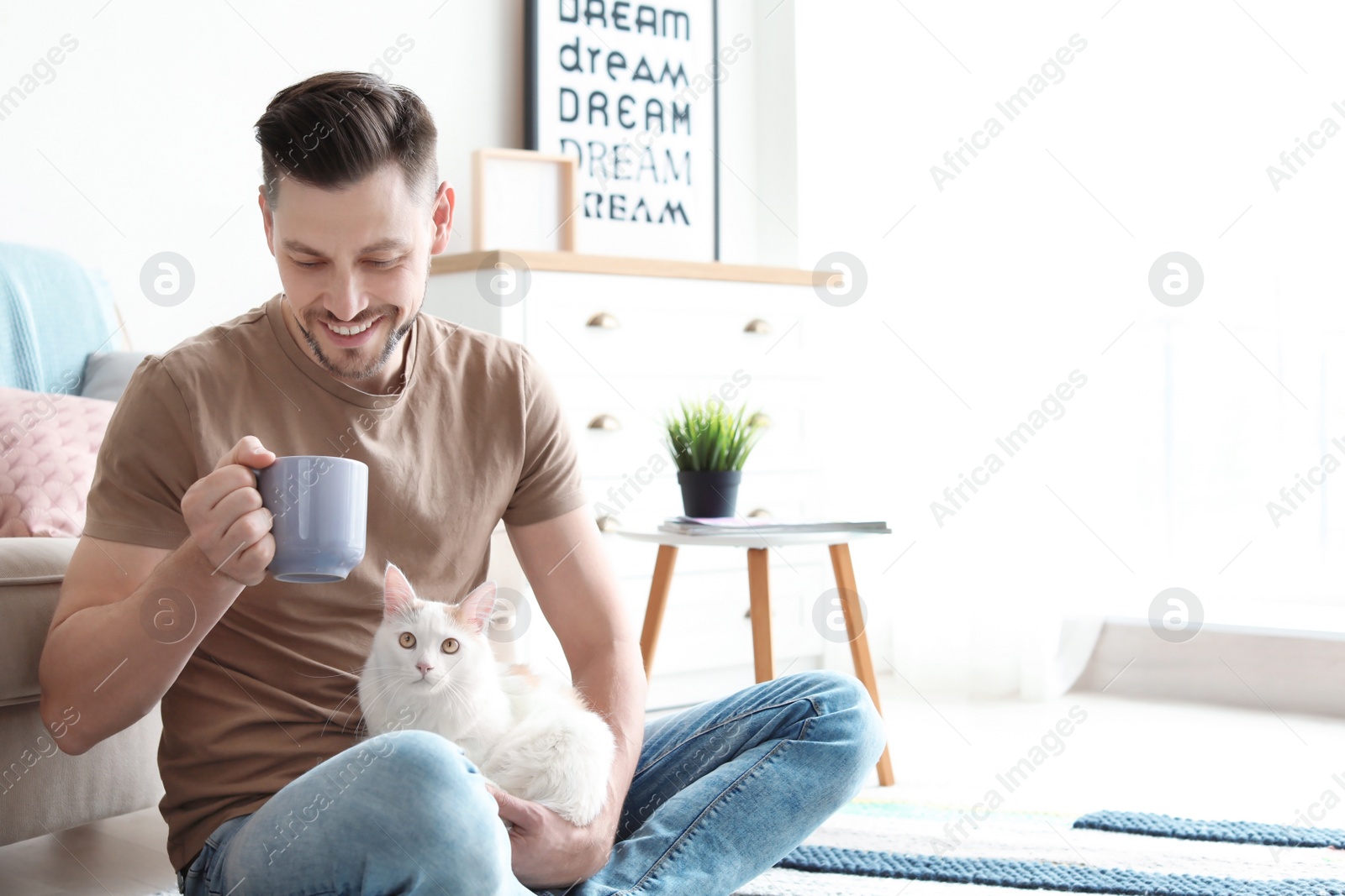 Photo of Young man with cute cat sitting on floor at home