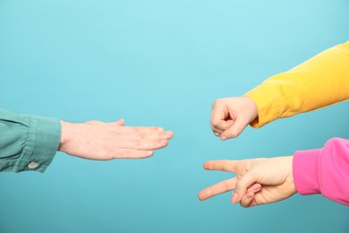 People playing rock, paper and scissors on light blue background, closeup