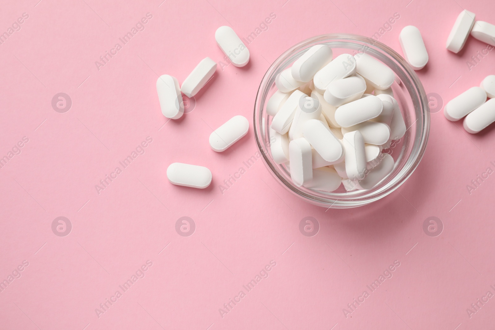 Photo of Vitamin capsules in bowl on pink background, top view. Space for text