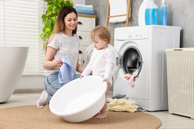 Photo of Happy mother with her daughter putting baby clothes into washing machine in bathroom