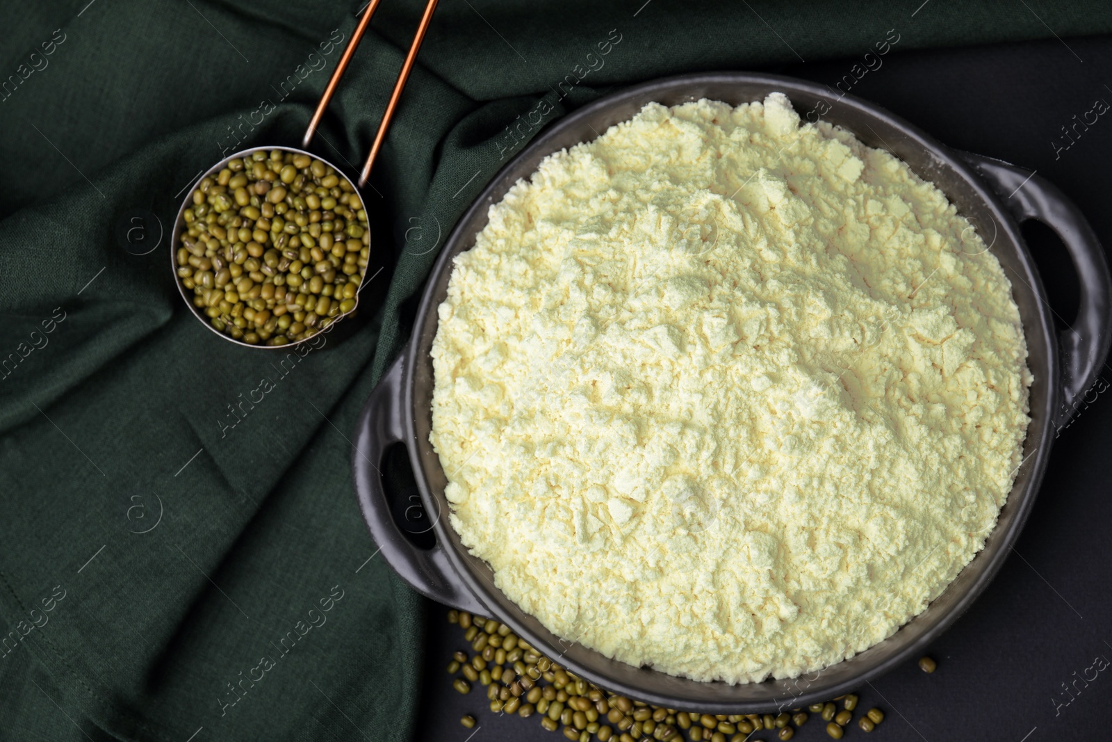 Photo of Pan with flour, mung beans and cloth on black background, flat lay