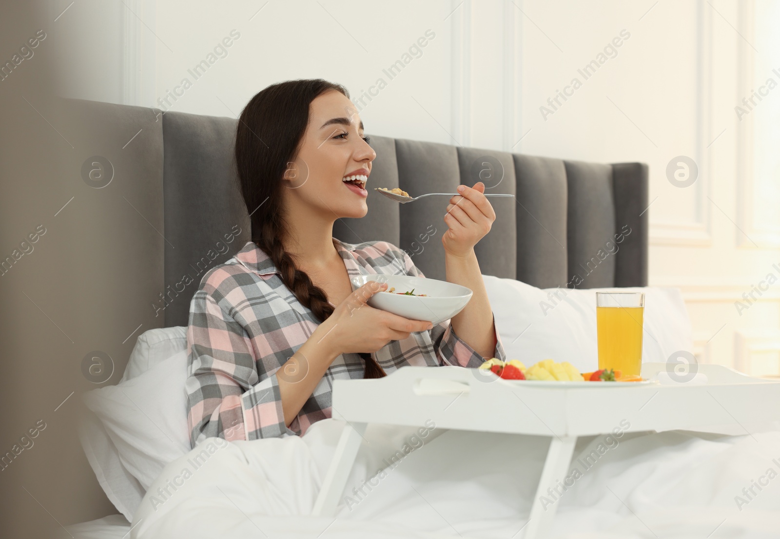 Photo of Happy young woman having breakfast on bed at home