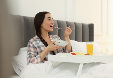 Happy young woman having breakfast on bed at home