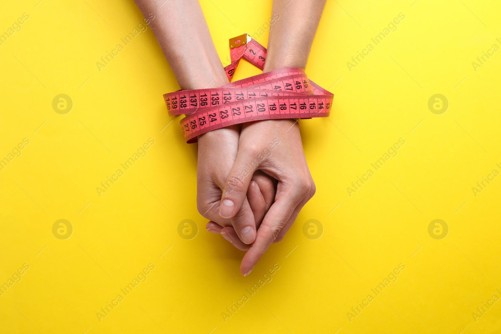 Photo of Woman tied with measuring tape on yellow background, top view. Diet concept