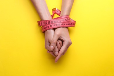 Woman tied with measuring tape on yellow background, top view. Diet concept