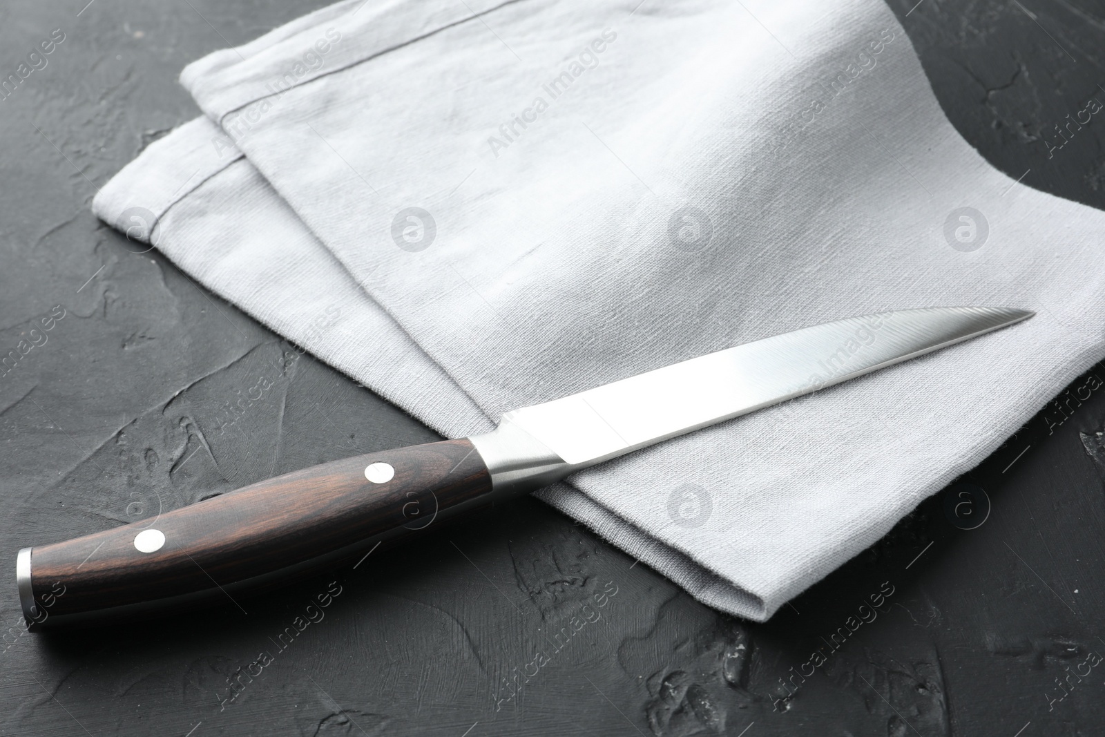 Photo of One sharp knife and napkin on dark textured table, closeup