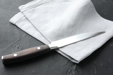 Photo of One sharp knife and napkin on dark textured table, closeup