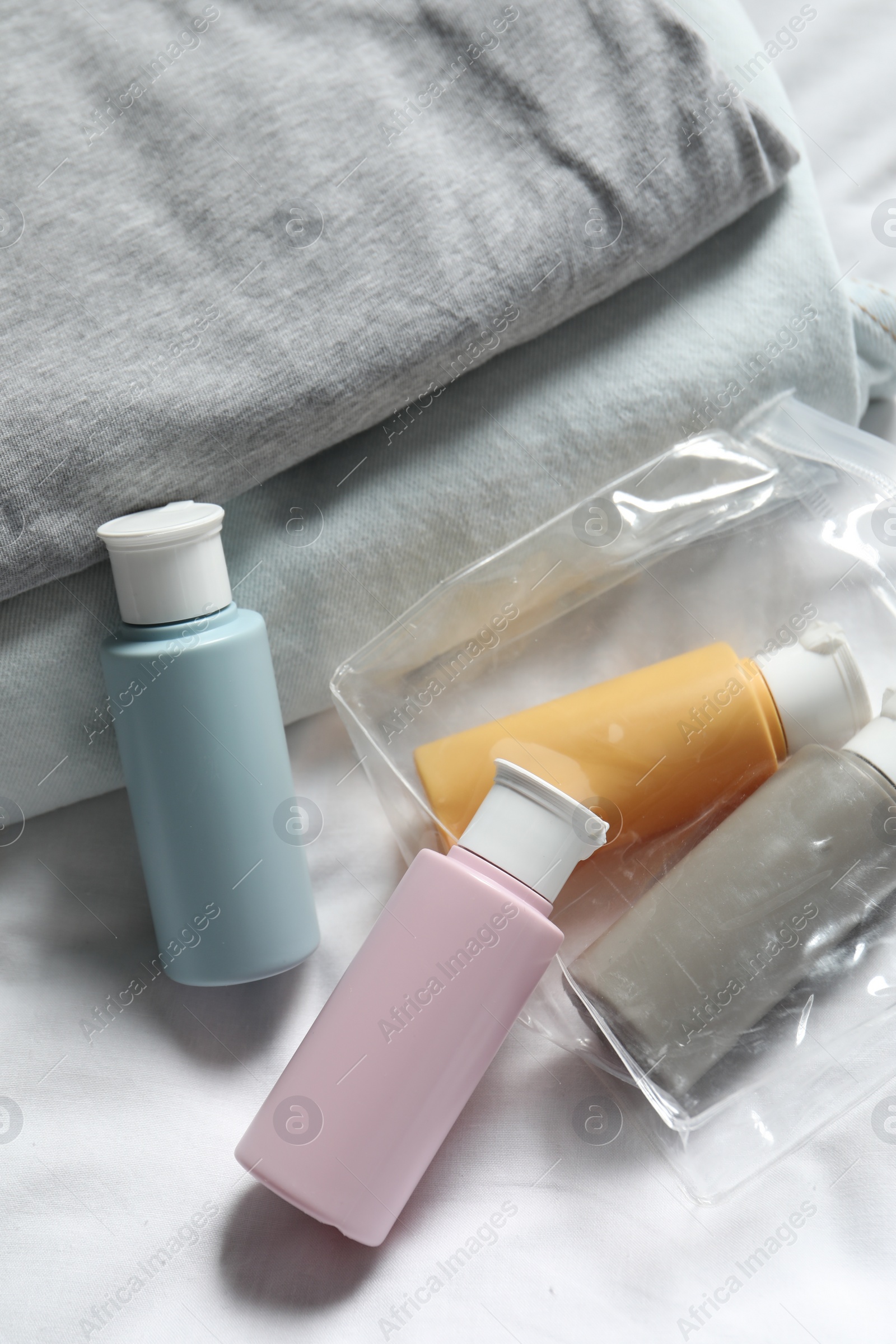 Photo of Cosmetic travel kit. Plastic bag with small containers of personal care products and stack of clothes on bed