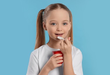 Photo of Cute little girl eating tasty yogurt on light blue background