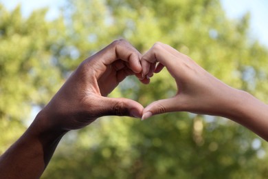 Photo of Woman and African American man making heart with hands outdoors, closeup