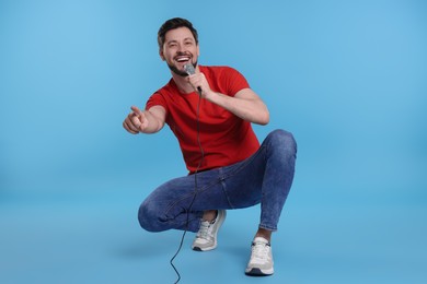 Photo of Handsome man with microphone singing on light blue background