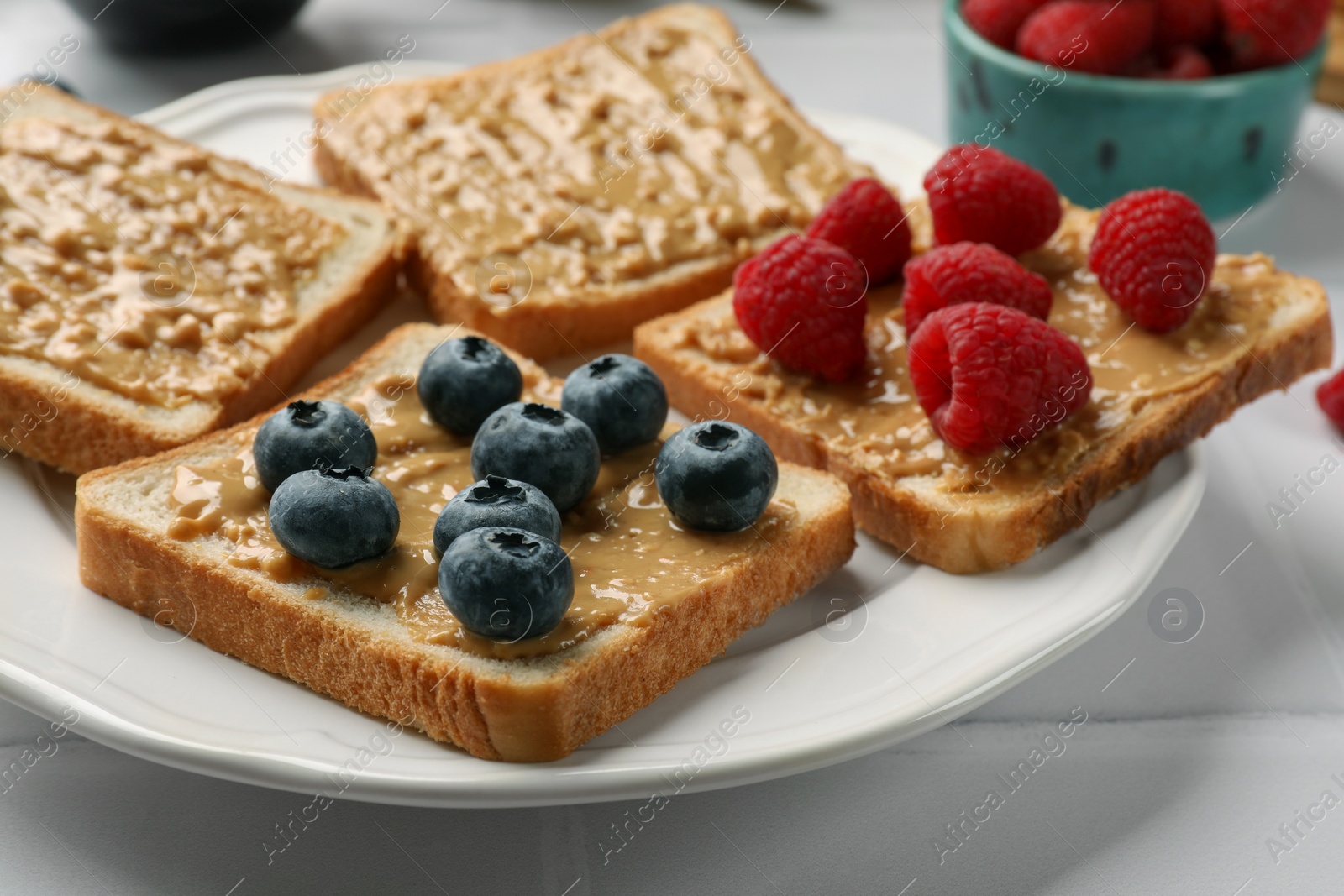 Photo of Delicious toasts with peanut butter, raspberries and blueberries on white table, closeup