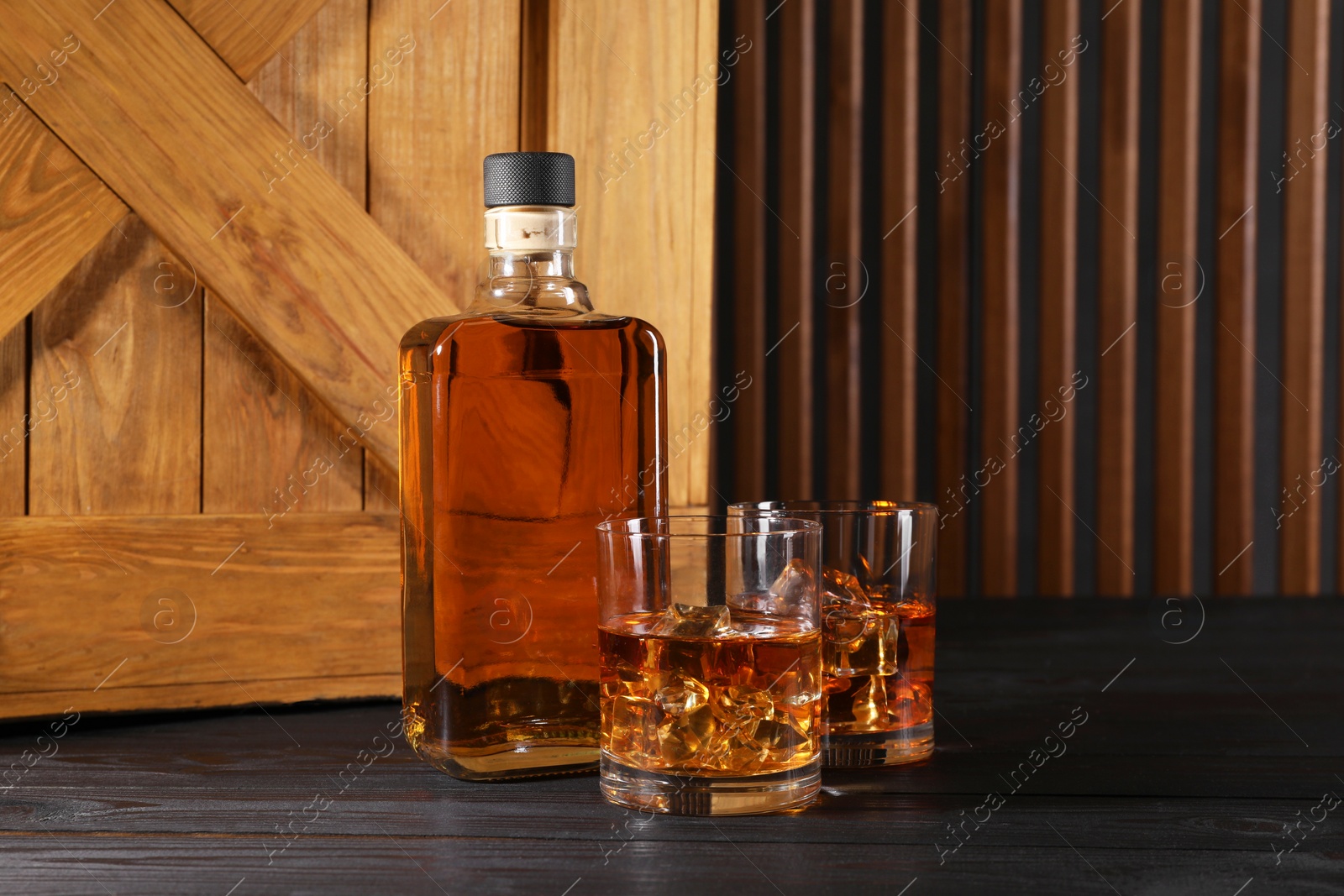 Photo of Whiskey with ice cubes in glasses and bottle on black wooden table