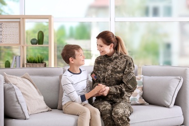 Woman in military uniform with her little son on sofa at home