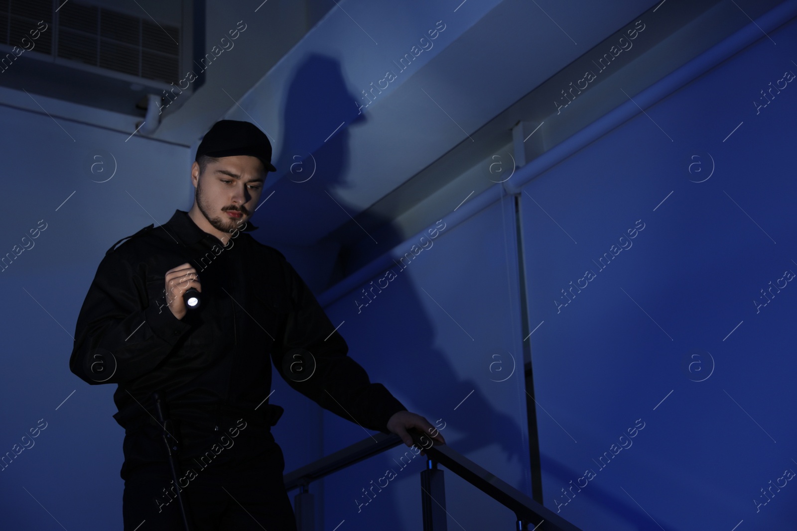 Photo of Male security guard with flashlight on stairs in darkness