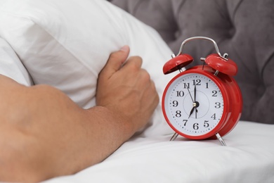 Alarm clock and man covering head with pillow in bedroom. Time of day