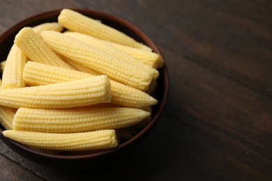 Photo of Tasty fresh yellow baby corns in bowl on wooden table, closeup. Space for text