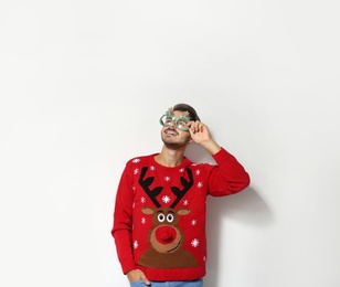 Young man in Christmas sweater with party glasses on white background