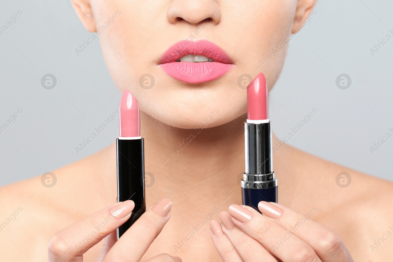 Photo of Young woman with lipsticks on gray background, closeup