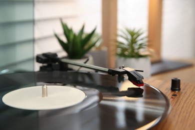 Photo of Stylish turntable with vinyl record on wooden table indoors, closeup