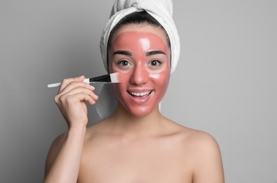 Woman applying pomegranate face mask on grey background