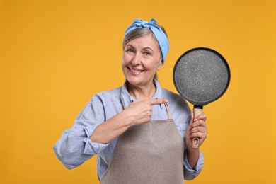Photo of Happy housewife with frying pan on orange background