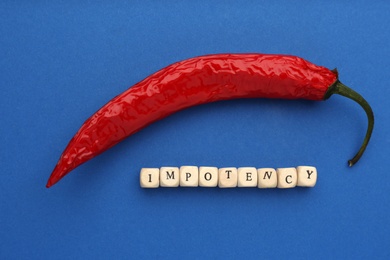 Photo of Chili pepper and cubes with word Impotency on blue background, flat lay