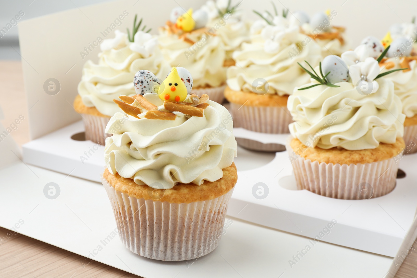 Photo of Tasty Easter cupcakes in box on wooden table, closeup