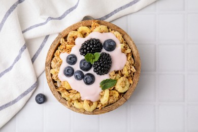 Photo of Tasty granola, yogurt and fresh berries in bowl on white tiled table, top view. Healthy breakfast