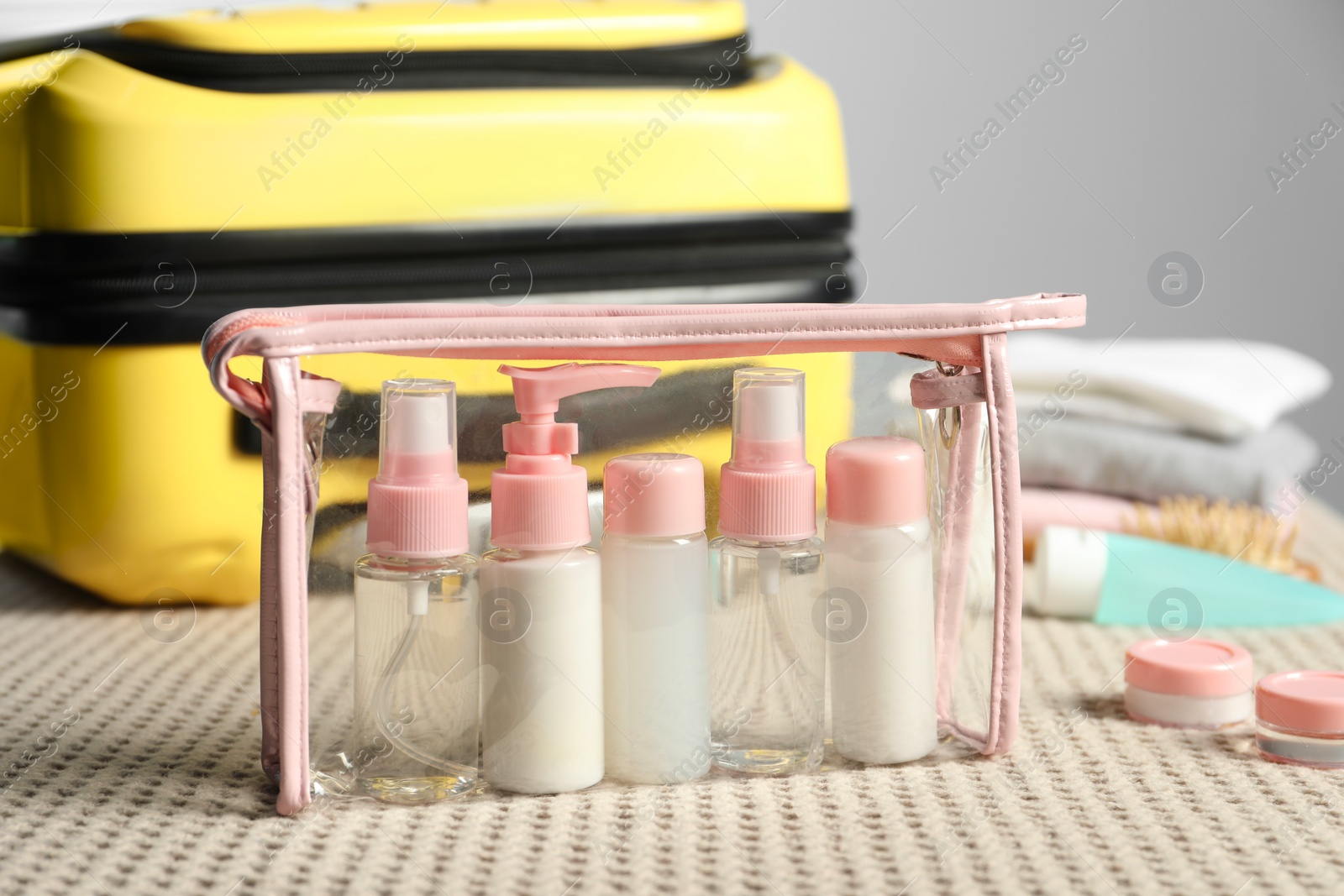 Photo of Plastic bag of cosmetic travel kit near suitcase on bed