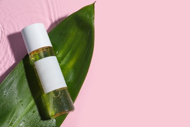 Photo of Bottle of cosmetic oil and green leaf in water on pink background, flat lay. Space for text