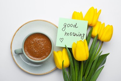 Photo of Cup of aromatic coffee, beautiful yellow tulips and Good Morning note on white background, flat lay