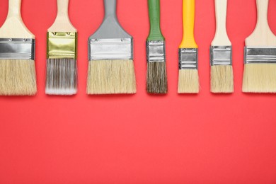 Photo of Many different paint brushes on red background, flat lay. Space for text