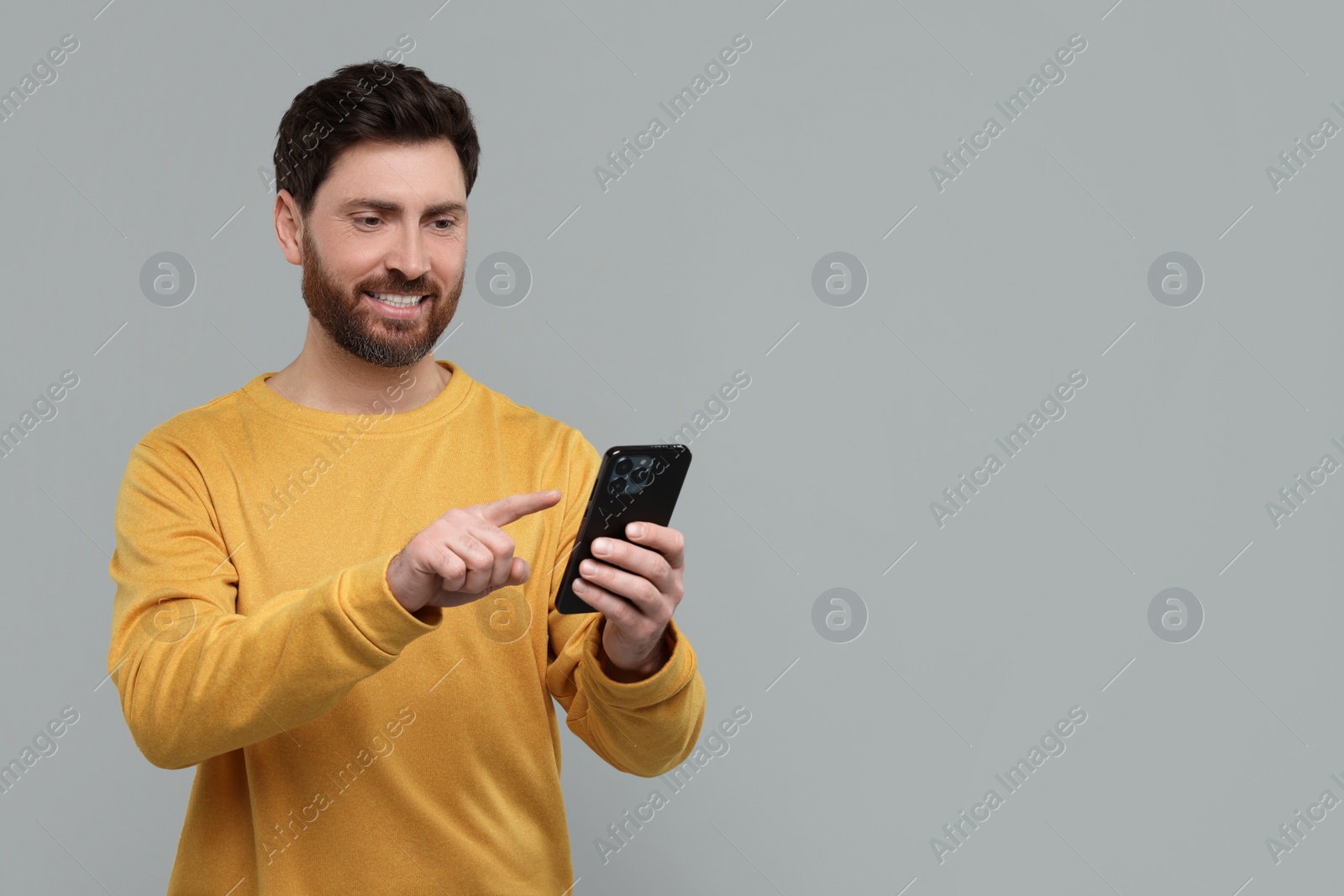 Photo of Smiling man with smartphone on grey background. Space for text